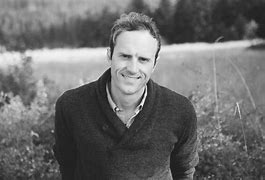 black and white image of a man standing in front of a neutral background, smiling